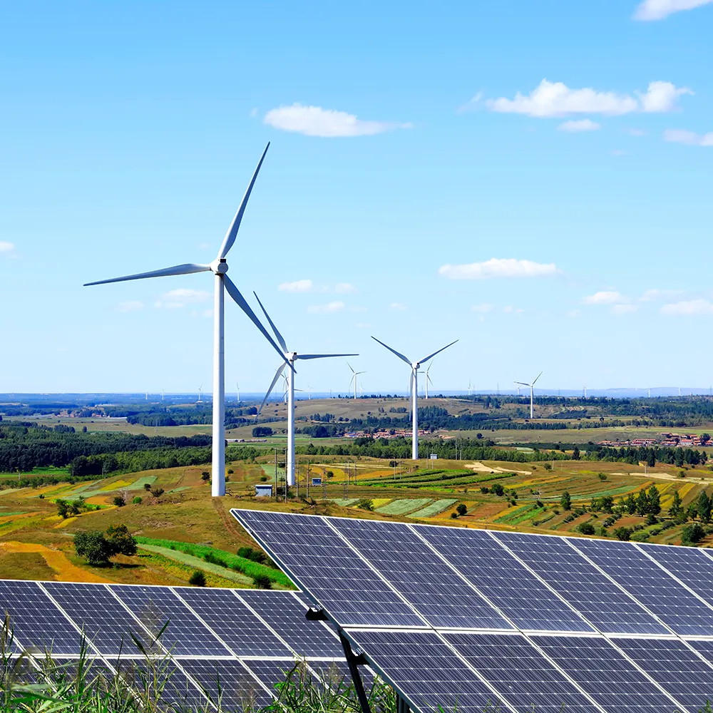 Landscape with large solar panels in the foreground and multiple wind turbines across rolling green fields under a clear blue sky, representing renewable energy.