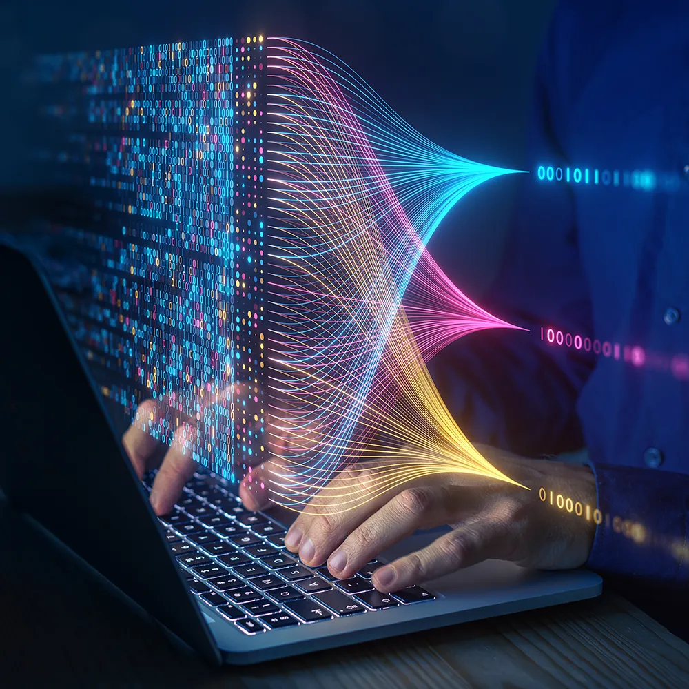 Person typing on a laptop with colourful digital data streams and binary code visualised flowing across the screen, representing analytics and advanced technology.