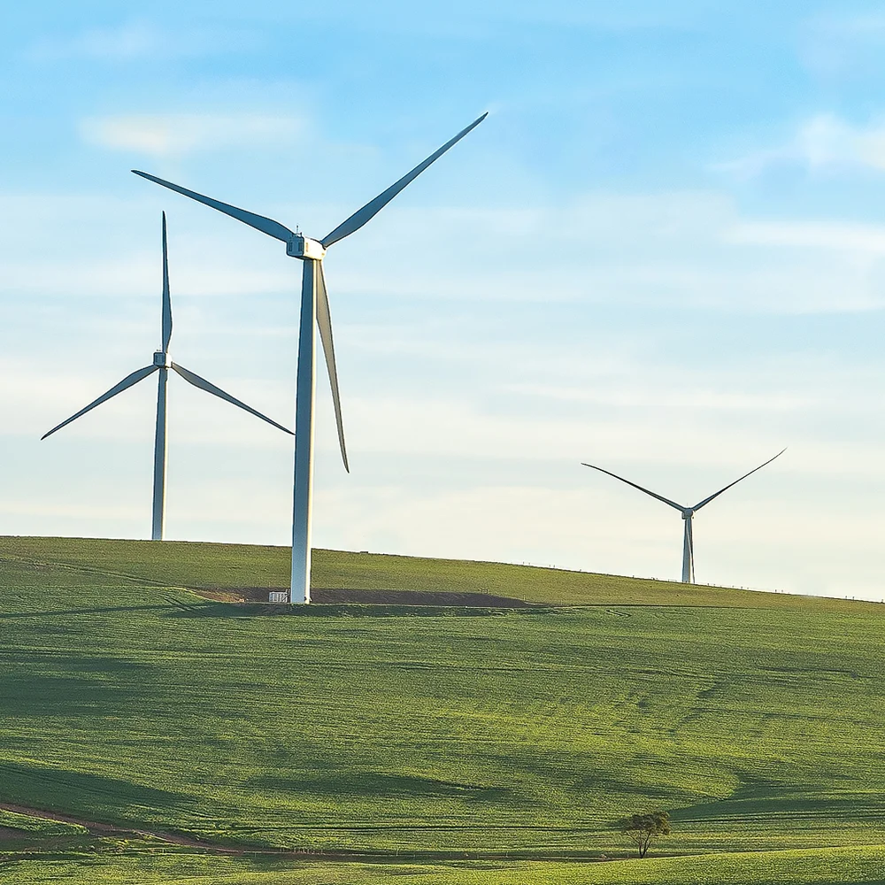 Three modern wind turbines on a gently rolling green field under a clear sky, viewed at an angle that emphasises their height and motion.